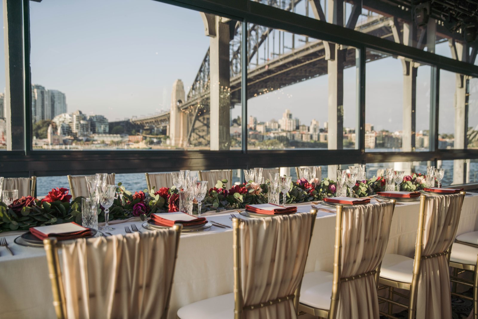 A long gala dinner table dressed with florals beside windows facing the Sydney Harbour Bridge